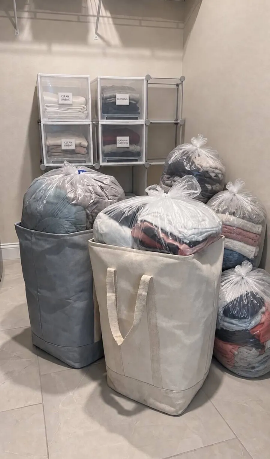 Bagged clean laundry organized in totes beside labeled linen and clothing bins